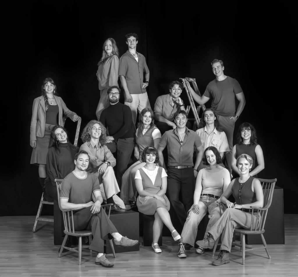 Gruppbild i svartvitt på hela klassen år 2025-2028 från Musikalakademien. Vissa sitter på stolar, vissa sitter på svarta kuber och vissa står på stolar. Svart ridå bakom.