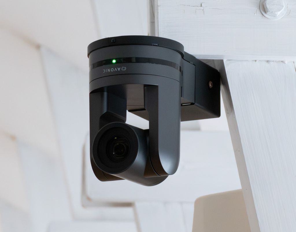 Bild på videomöteskamera som sitter i taket. Taket är ljust med träbalkar.